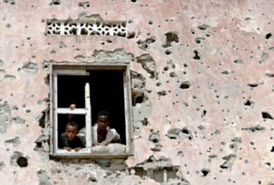 طفلان صوماليان ينظران من نافذة منزلهما المدمر إلى جموع المتظاهرين من أجل السلام في يوليو الماضي بمقديشو