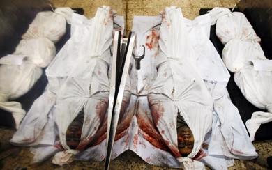 جثة الصحفي الفلسطيني إيهاب الوهيدي (وسط) إلى جانب جثة شهيد آخر على الأرض بمشرحة مستشفى بغزة أمس
