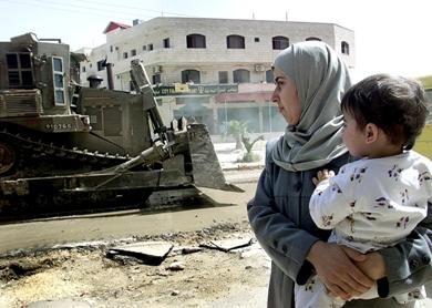 صورة تعود إلى 11 أبريل 2002 لامرأة فلسطينية حاملة طفلها تمر من أمام جرافة للجيش الإسرائيلي في بلدة جنين بالضفة الغربية