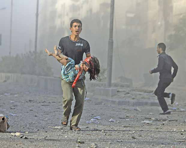 سوري يحمل طفلة مصابة بعد الغارات الجوية على المناطق السكنية في مدينة دوما 