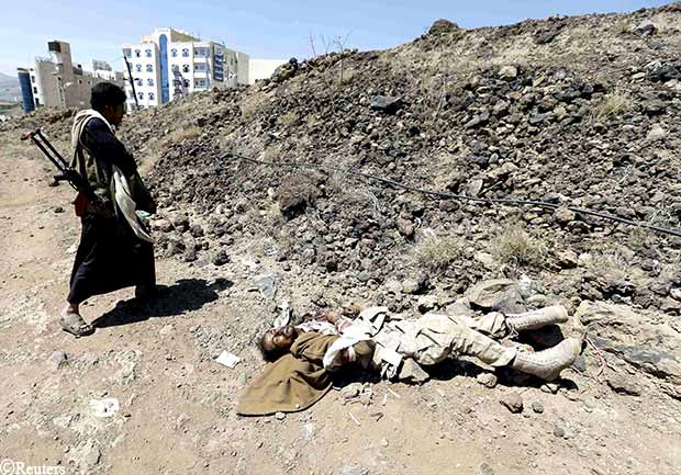 أحد مقاتلي الحوثي يمشي بجانب جثة جندي يمني قتل في معارك الفرقة الأولى مدرع أمس الأول