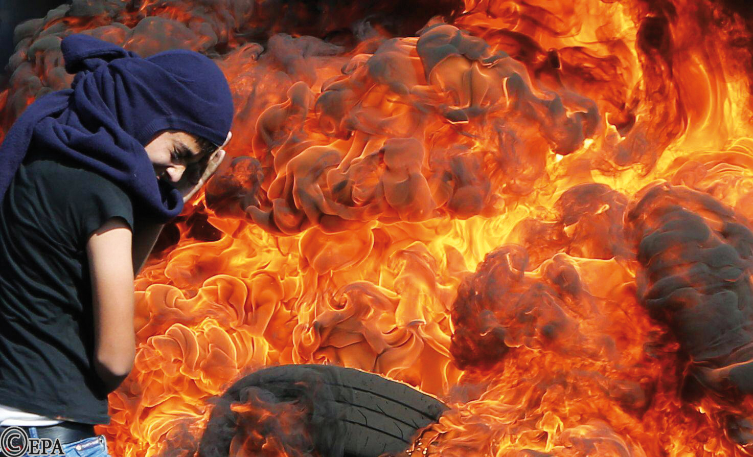 فلسطيني يحمي وجهه بينما يقف بجانب إطارات تحترق خلال احتجاجات أمس في قرية كفر قادوم قرب نابلس