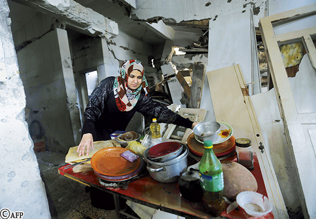 غزاوية تغسل القدور والأطباق في منزلها المدمر حيث تعيش وعائلتها في منطقة الشجاعية أمس
