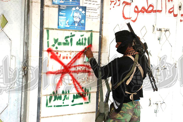 احد أبطال المقاومة يقوم بطمس شعار الحوثيون من الجدار