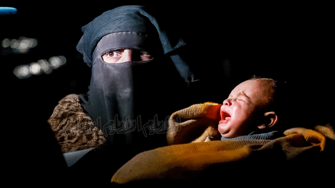 امرأة ترتدي النقاب تحمل طفلاً رضيعًا بالقرب من حفل نفط عمر في ريف محافظة دير الزور