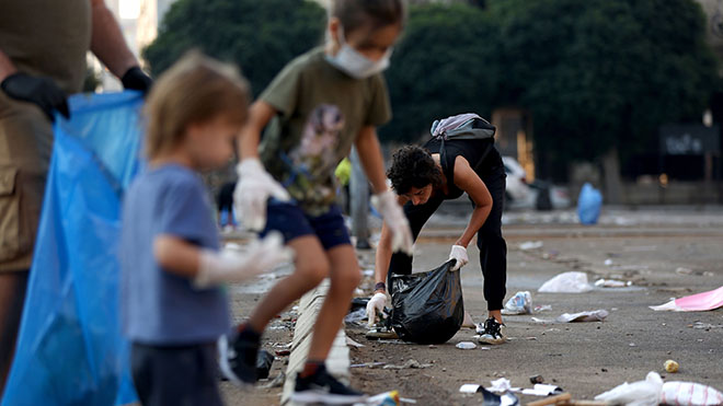 أطفال يساعدون اللبنانيين في المجتمع المدني على إزالة القمامة في أحد شوارع وسط العاصمة بيروت بعد ليلة من الاحتجاجات