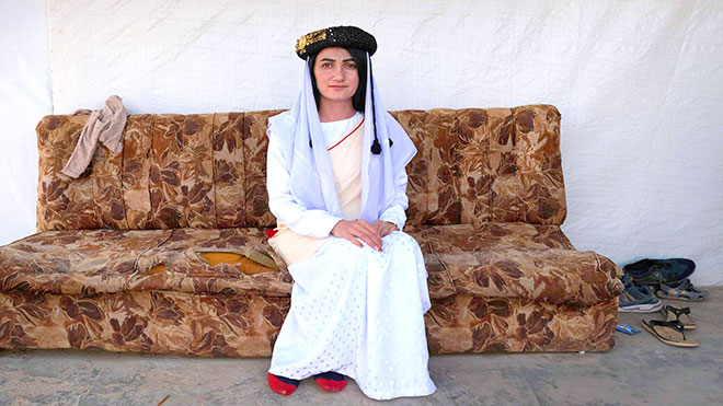 إيمان عباس ، وهي امرأة يزيديّة تبلغ من العمر 18 عامًا ترتدي الزي التقليدي ، تُصور أمام خيمة في مخيم شعيرة للنازحين