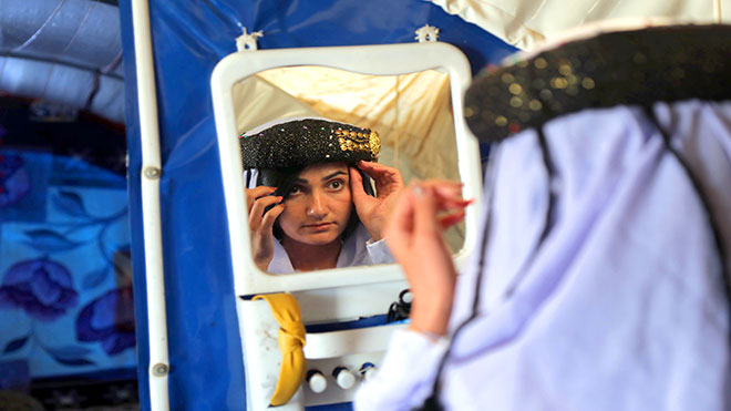 إيمان عباس ، وهي امرأة يزيديّة تبلغ من العمر 18 عامًا ترتدي الزي التقليدي ، تنظر إلى نفسها داخل مرآة داخل خيمة في مخيم الشراع للنازحين