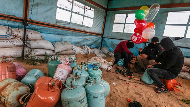 فلسطينيون ملثمون يضخّمون البالونات ، التي سيتم ربطها بعد ذلك بعبوة غاز ستكون بمثابة أداة حارقة