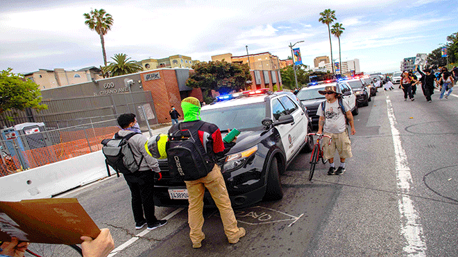 متظاهرون يقفون أمام سيارة للشرطة أثناء سيرهم باتجاه وسط مدينة لوس أنجلوس بعد أن تظاهروا في حي بويل هايتس في لوس أنجلوس