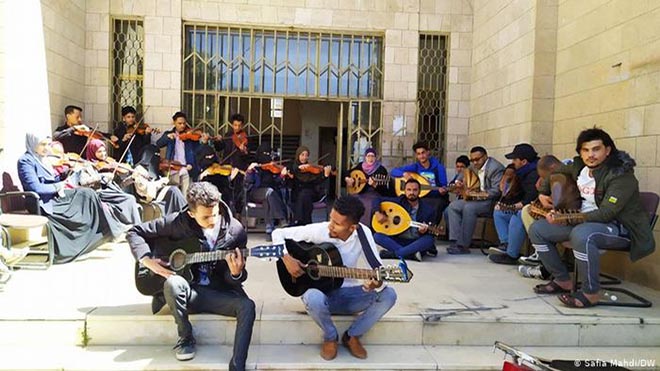 فتيان وفتيات يمنيات أمام المركز الثقافي في العاصمة صنعاء خلال أداء معزوفة موسيقية في ظل أوضاع الحرب القاسية