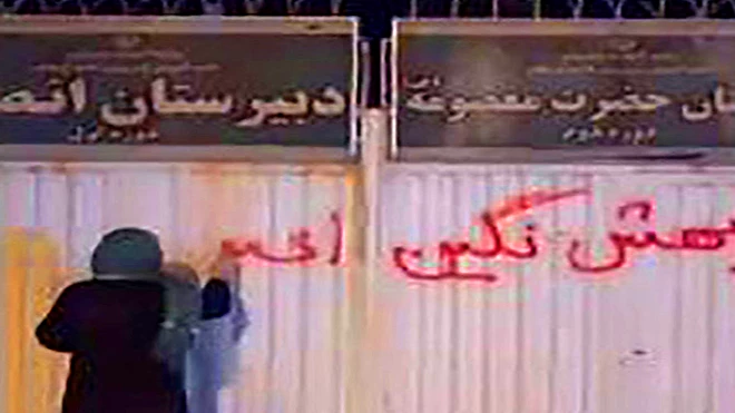 فتاة تخط على جدار مدرسة للفتيات في مدينة زنجان شمال إيران عبارة "لا تسمّوها احتجاجات، إنها ثورة" (غيتي)