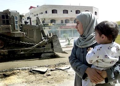 صورة تعود إلى 11 أبريل 2002 لامرأة فلسطينية حاملة طفلها تمر من أمام جرافة للجيش الإسرائيلي في بلدة جنين بالضفة الغربية