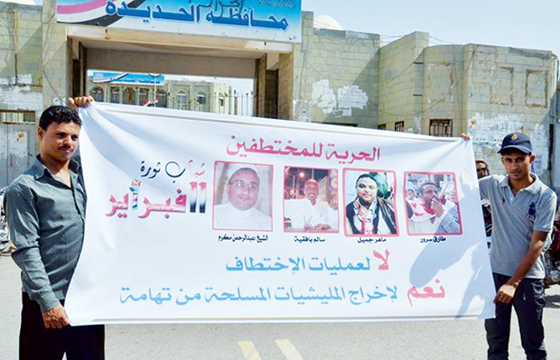 شابان يحملان لافتة لصور بعض المختطفين في تهامة