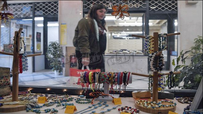 ابة تنظر إلى مجوهرات مصنوعة يدوياً في متجر افتتحه مشروع ليالي بالتعاون مع بلدية أثينا لبيع الحرف اليدوية التي صنعها اللاجئون ابة تنظر إلى مجوهرات مصنوعة يدوياً في متجر افتتحه مشروع ليالي بالتعاون مع بلدية أثينا لبيع الحرف اليدوية التي صنعها اللاجئون